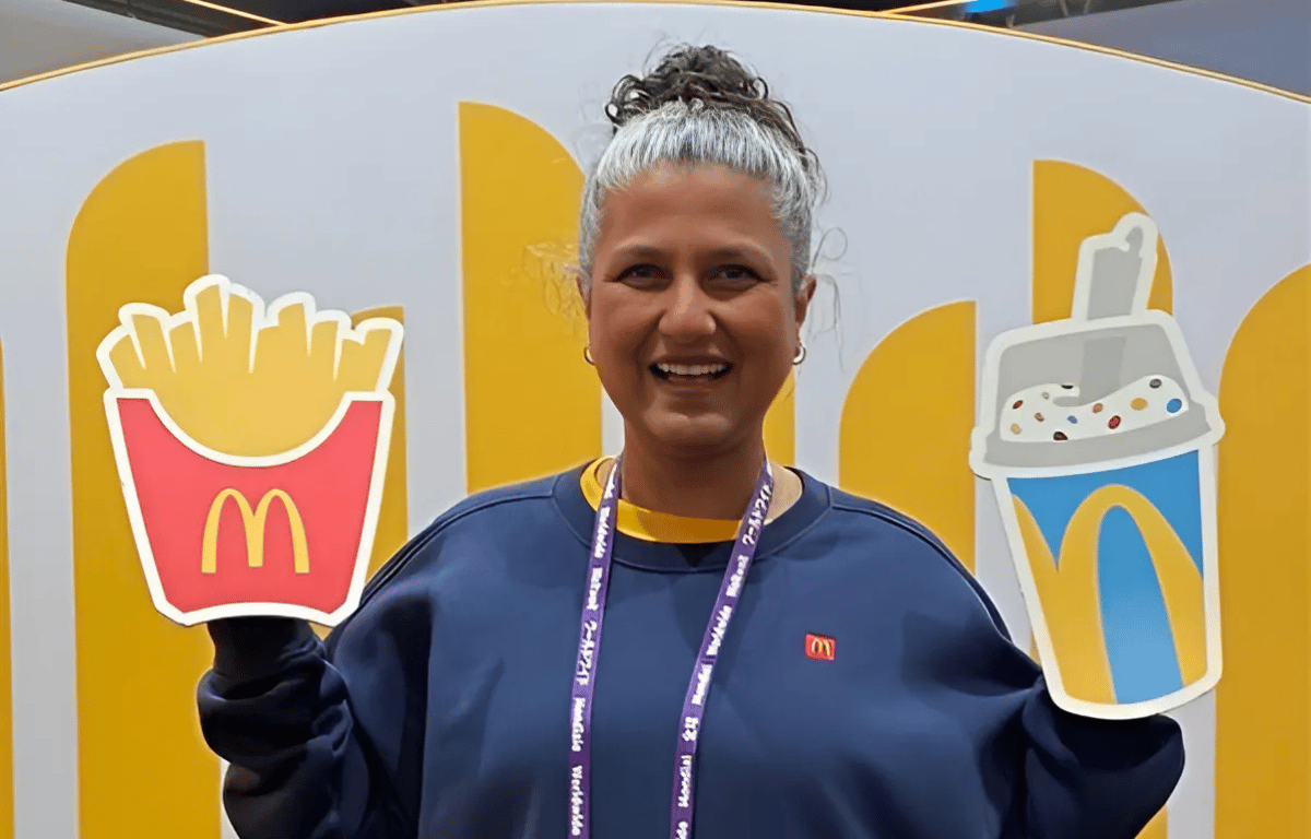 Bindu Rivas, McDonald's uniform designer, holds McDonald's food icon signs at the 2024 worldwide convention, symbolizing her integral role in connecting innovative uniform designs with the brand's iconic identity.